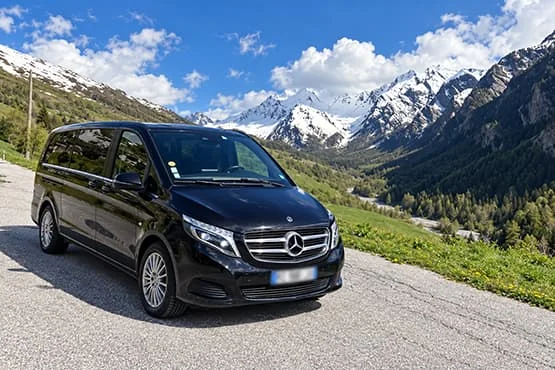 Van Mercedes noir sur une route devant des sommets enneigés.